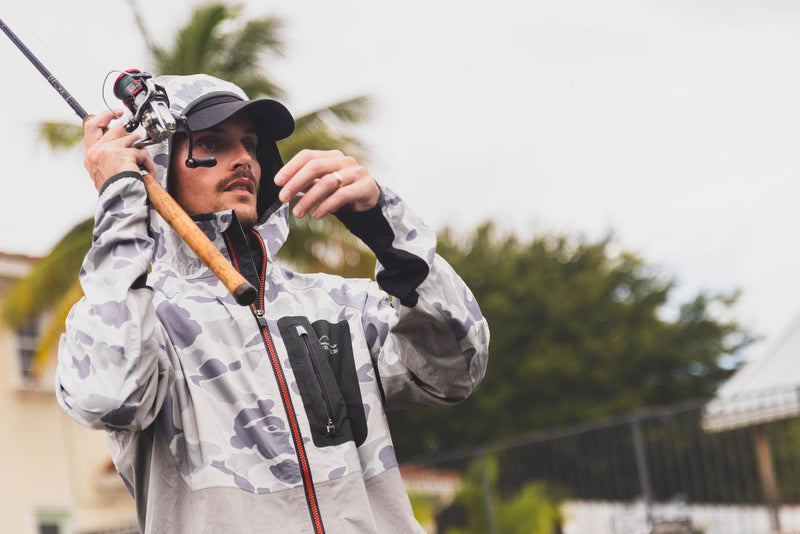 Man holding a fishing pole wearing the Ultra-Lite Backwaters Waterproof Stretch Jacket, showcasing its lightweight, waterproof design ideal for outdoor activities.