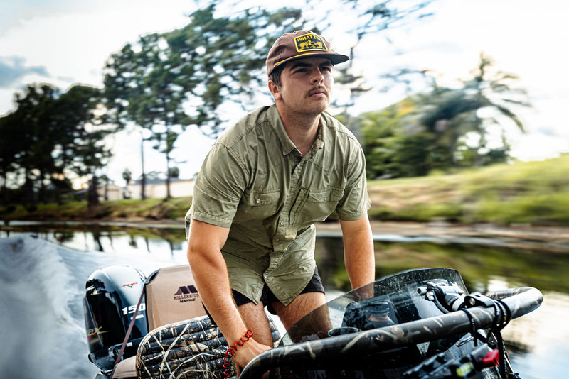 Young man steering a boat, wearing the Drake Cinco Ranch Western Acid Washed Short Sleeve Shirt, showcasing its classic western fit and functional design elements.