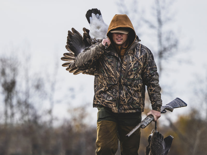 Hunter in camouflage with the LST BMF 3-in-1 Pit Jacket, carrying geese and a shotgun, showcasing durable, versatile hunting gear from Purewhitelaneshop.