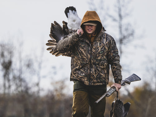 Hunter in camouflage with the LST BMF 3-in-1 Pit Jacket, carrying geese and a shotgun, showcasing durable, versatile hunting gear from Purewhitelaneshop.