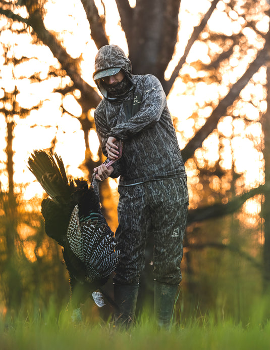 Man in camouflage holding a turkey, showcasing the Men's Turkey Pant with Spider Web Technology designed for enhanced mobility and silent hunting.