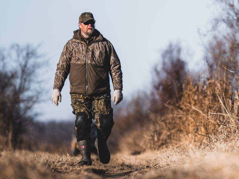 Man in LST BMF Eqwader Full Zip with Primaloft walks through dry field, showcasing its durability and weather protection for outdoor adventures.