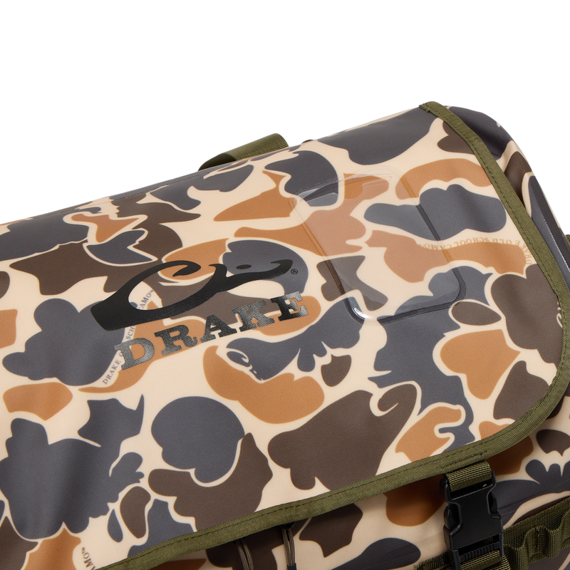 Close-up of a Drake Waterproof Duffel Bag with camouflage pattern, olive-green trim, black buckle, and logo on top flap, featuring durable construction and convenient pockets.