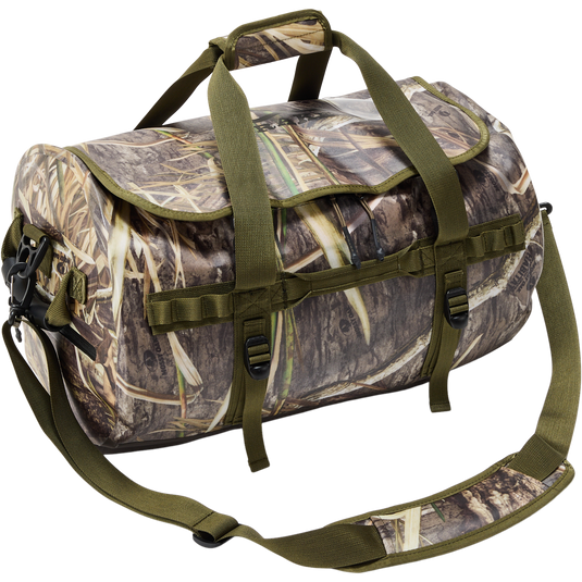 Waterproof Duffel Bag with marsh-grass camouflage, olive-green handles, adjustable strap, attachment loops, and compression straps, designed for outdoor and hunting gear storage.