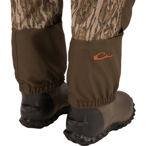 Hardline Uninsulated Breathable Wader with elasticized cuffs over waterproof rubber boots, featuring durable three-layer fabric and orange logo, ideal for outdoor adventures.