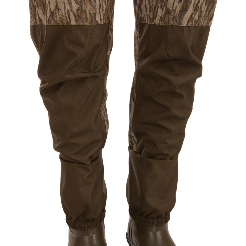 Hardline Uninsulated Breathable Wader featuring camouflage-pattern, waterproof design with ankle cinch, worn over dark rubber boots, ideal for outdoor adventures and hunting.