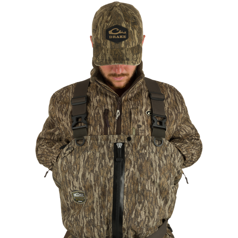 Man wearing Insulated Guardian Elite HND Front Zip Wader, featuring a camouflage jacket and hat, designed for warmth, durability, and waterproof protection.