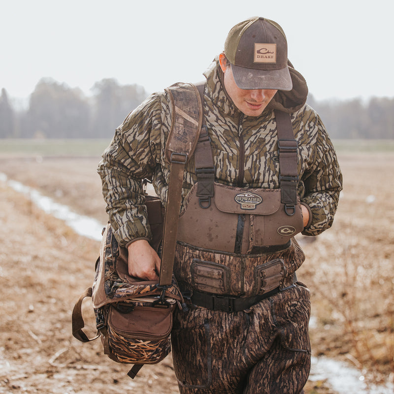 A man in the field with hat and bag, showcasing the Buckshot Eqwader 1600 Neoprene Wader 3.0 by Purewhitelaneshop, designed for top-tier waterfowl hunting with advanced features for comfort and durability.