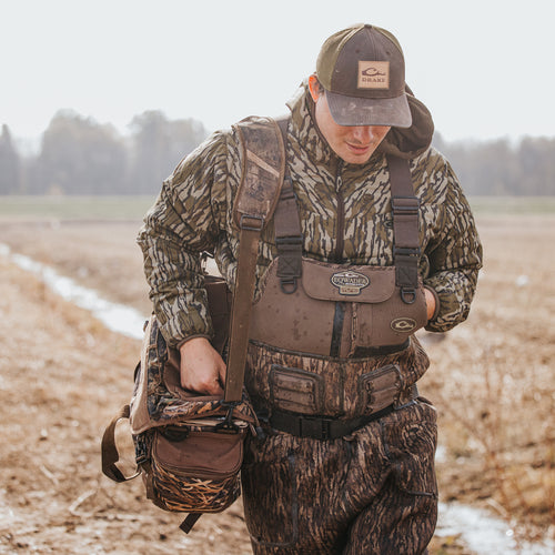 A man in the field with hat and bag, showcasing the Buckshot Eqwader 1600 Neoprene Wader 3.0 by Purewhitelaneshop, designed for top-tier waterfowl hunting with advanced features for comfort and durability.