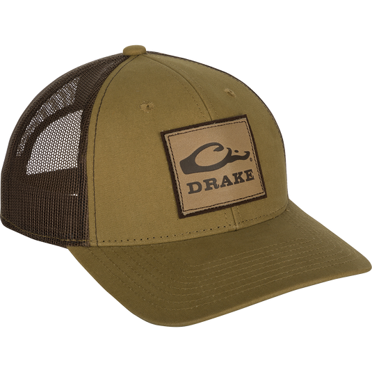 A weathered cotton/poly structured cap with a leather patch featuring the Drake Logo. Traditional trucker shape with a pre-curved visor and adjustable snapback closure. 