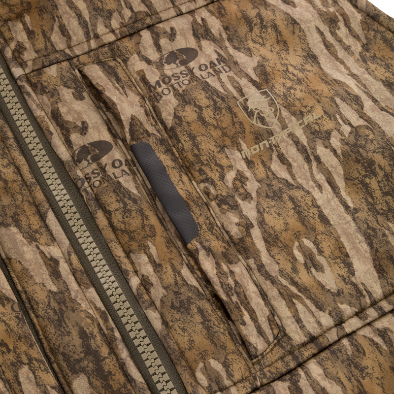 Close-up of the Midweight Nova Silencer Vest with Agion Active X2, featuring a chunky zipper, welted pocket, and Mossy Oak Bottomland camo with brand logos.