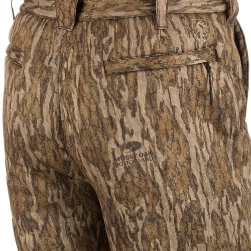 Close-up of Midweight Nova Silencer Pant with Scent Control in Mossy Oak Bottomland pattern, featuring zippered pockets, belt loops, and stretch waistband for mobility.
