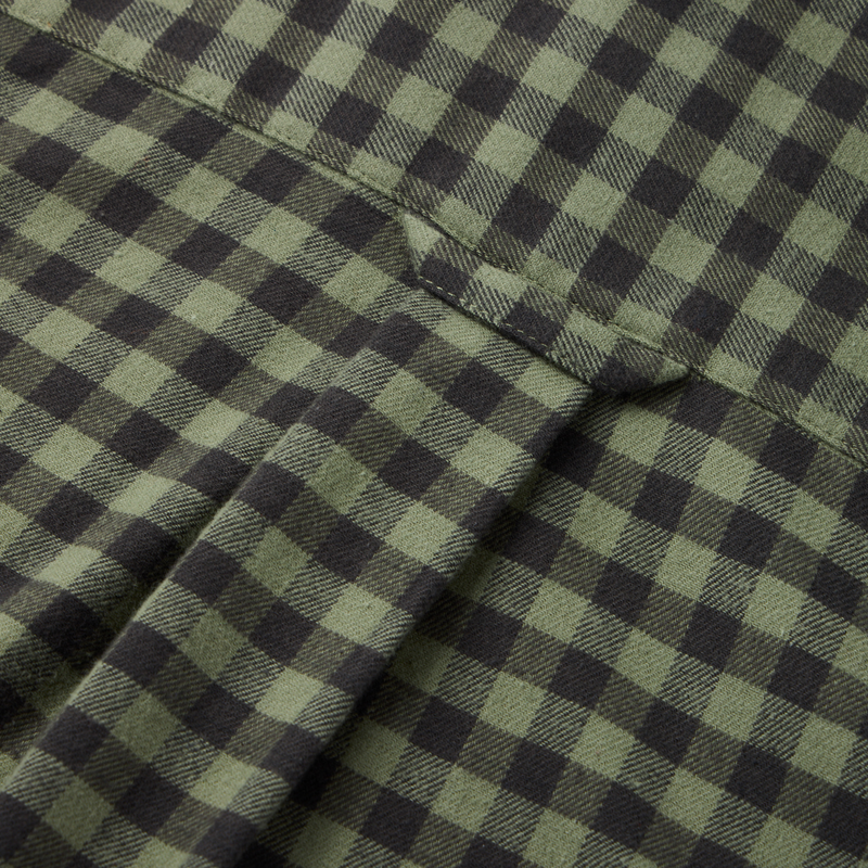Close-up of the Autumn Flannel Shirt's green and black checkered fabric, showcasing the seam and flap of its patch pocket, emphasizing its outdoor lifestyle design.