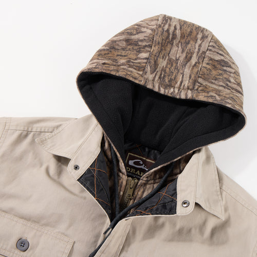 Campfire Canvas Shirt Jac Hoodie with beige shell, camo hood, black fleece lining, snap buttons, and chest pocket, suitable for versatile wear in cool weather.