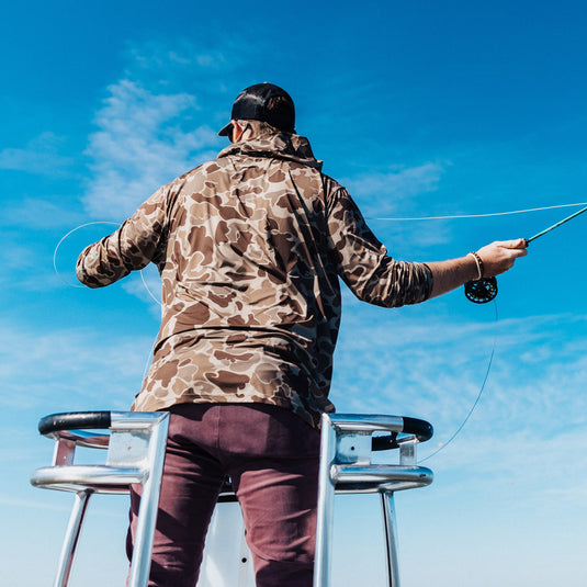 A man on a boat holding a fishing pole, wearing the Hunter Creek Old School Bamboo Long Sleeve Hoodie by Purewhitelaneshop. Lightweight, odor-resistant, with UPF 20 sun protection.