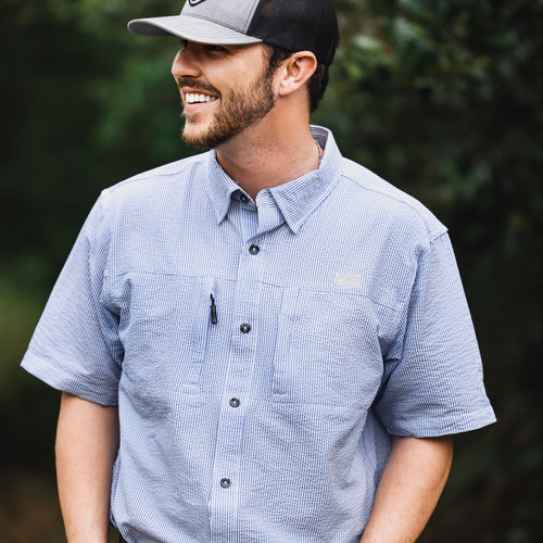 A man in a Classic Seersucker Stripe Button-Down Short Sleeve Shirt with button-down collar, chest pockets, and vented cape back, embodying Purewhitelaneshop's high-quality hunting and casual apparel.