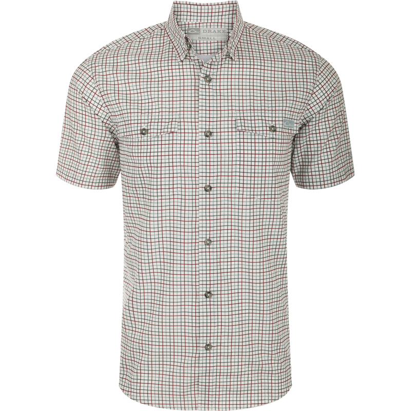 A close-up of the Drake Frat Tattersall Shirt, featuring a white and red plaid pattern. The lightweight performance fabric offers UPF30 sun protection, moisture-wicking, and quick-drying properties. With a classic fit and hidden button-down collar, it also includes two button-through flap chest pockets, a vented cape back, and a sculpted hem. The shirt even has a built-in sunglass wipe. Perfect for big game hunting, waterfowl hunting, turkey hunting, fishing, and casual wear.