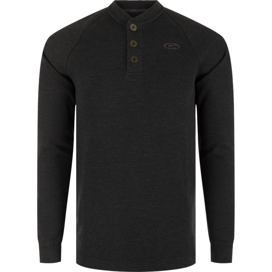 A black long sleeve Henley shirt with metal logo buttons, raglan sleeves, rib knit collar, and cuffs. Made of waffle mélange fabric for comfort, antimicrobial, and moisture-wicking properties. Split tail hem for versatile styling.