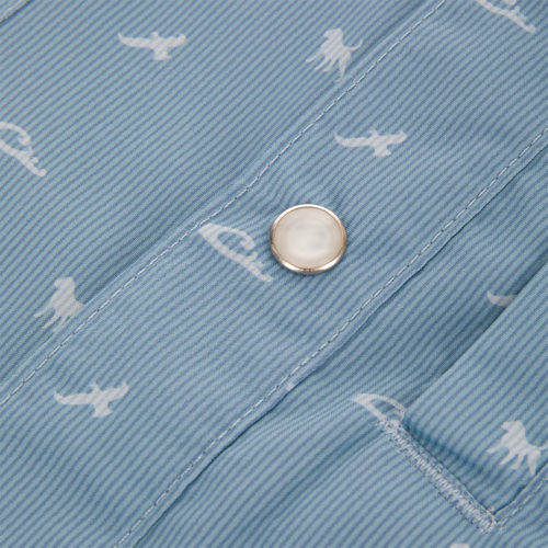 Close-up of Drake Cinco Ranch Western Short Sleeve Shirt, featuring light-blue striped fabric with white dinosaur silhouettes, metallic snap button, and edge of a stitched pocket.