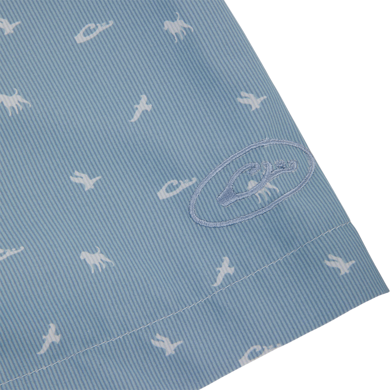 Close-up of the Cinco Ranch Western Short Sleeve Shirt featuring light-blue seersucker fabric with white prehistoric creature silhouettes and an embroidered logo on the hem.