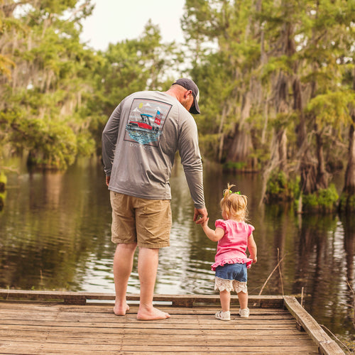 A man and child on a dock, the man wearing a Drake Icon Americana Long Sleeve Performance Crew, ideal for outdoor comfort with UPF 50 protection and quick-drying fabric.