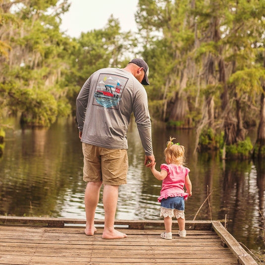 A man and child on a dock, the man wearing a Drake Icon Americana Long Sleeve Performance Crew, ideal for outdoor comfort with UPF 50 protection and quick-drying fabric.