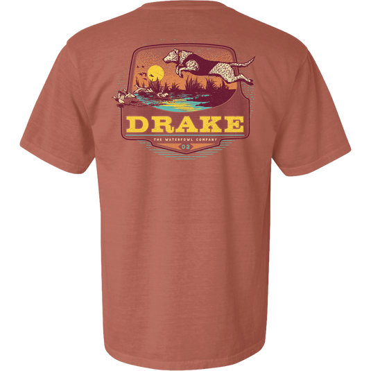 Don’t Let Em Behind You T-Shirt featuring a hunting dog graphic leaping over a marsh with ducks, sunset backdrop, and Drake logo on the back.