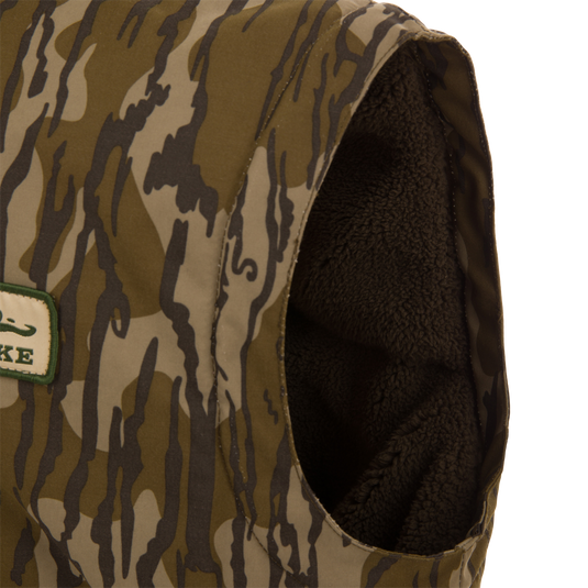 Throwback 80 Sport Vest, a sleeveless camo vest with fleece lining, features large pockets, brass zipper, and wind flap, ideal for outdoor adventures.