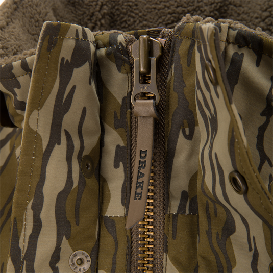 Close-up of the Throwback 80 Sport Vest’s tiger-stripe camouflage, highlighting the YKK zipper with leather pull embossed DRAKE and a peek of sherpa fleece lining.