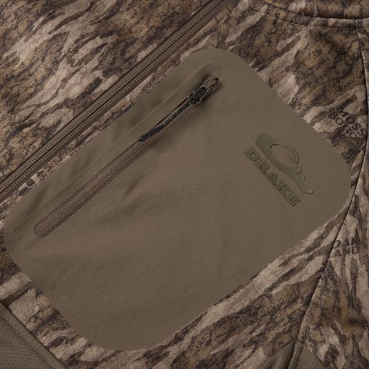 Close-up of MST Offset 2.0 Half Zip Hoodie's zippered, water-resistant chest pocket with Drake logo and Mossy Oak Bottomland camo, showcasing rugged outdoor design.
