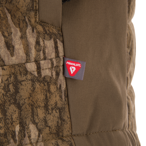 Close-up of LST BMF Jacket with Primaloft, showing a stitched tag on camouflage and olive-green fabric, highlighting its insulated, lightweight design for active use.