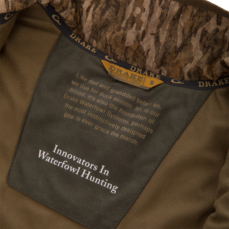 Inside view of Purewhitelaneshop LST BMF Vest with Primaloft, showcasing camo collar, size tag, and product slogan emphasizing innovation and warmth for hunting.