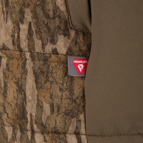 Close-up of the LST BMF Vest with PrimaLoft, featuring a camouflage and olive drab fabric with a red PrimaLoft tag, highlighting its insulated, lightweight, windproof design.