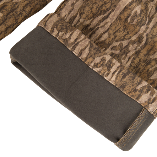 MST CommandXT Softshell Pant close-up, showing camouflage fabric with dark-grey fleece hem, highlighting flexible, windproof, water-resistant material designed for hunting and outdoor activities.