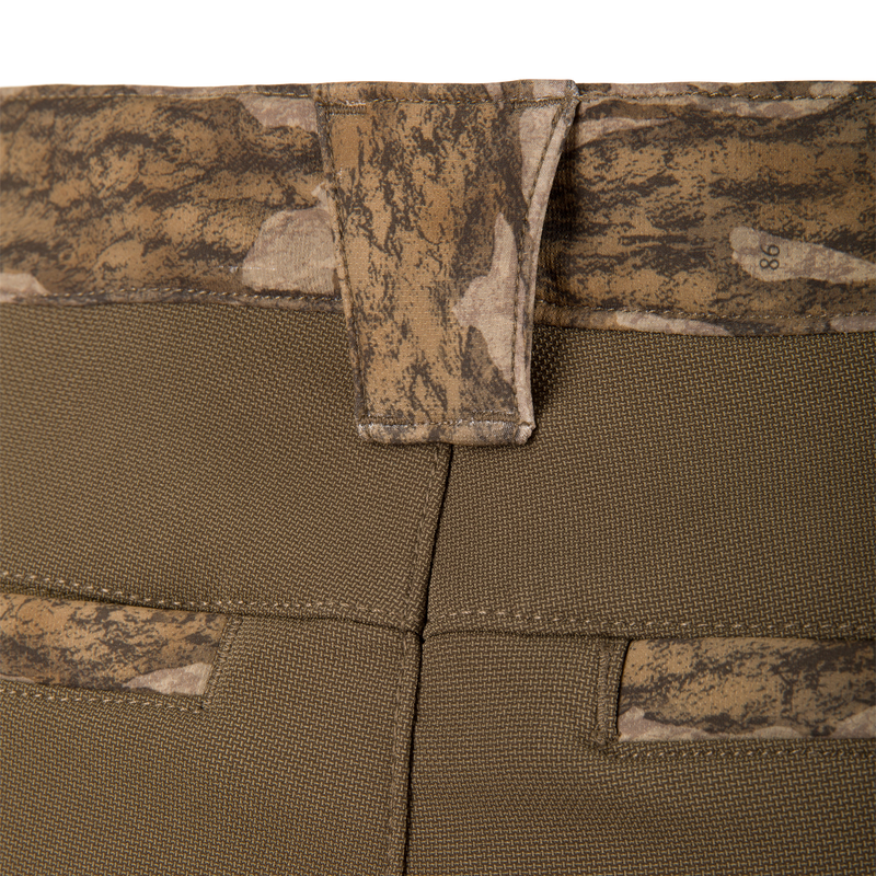 Close-up of the MST CommandXT Softshell Pant's waistband, highlighting camo-patterned inner lining, olive textured fabric, and a belt loop, emphasizing comfort and durability for demanding activities.