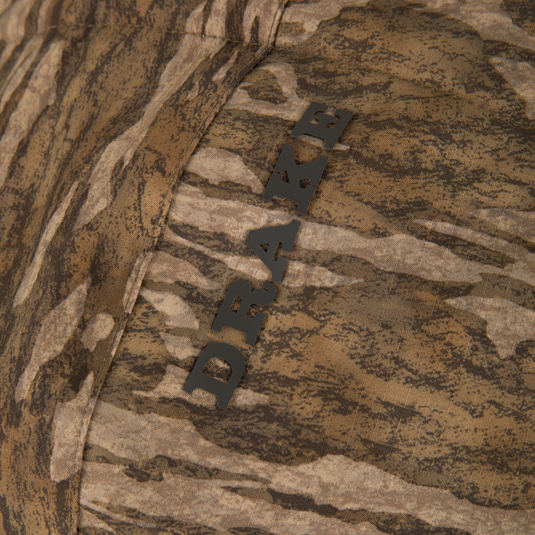 Close-up of the LST BMF Eqwader Full Zip with Primaloft, showcasing brown camouflage fabric and DRAMA metal tag, emphasizing waterproof, breathable, insulated outdoor performance.