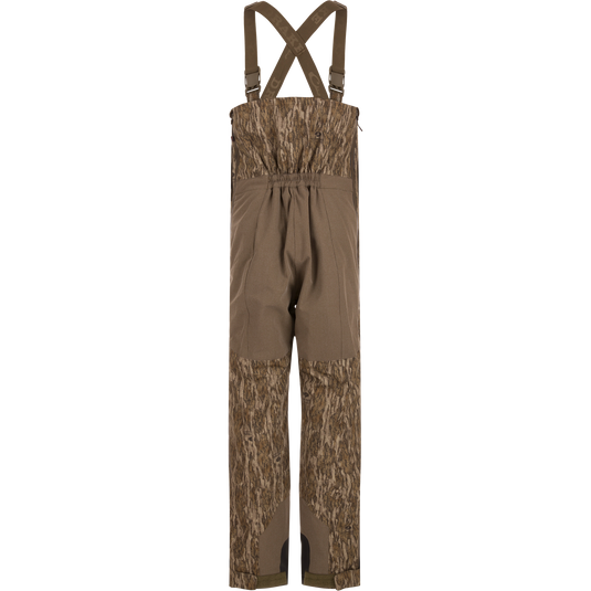 LST BMF Pit Bib with Primaloft: Camouflage bib pants featuring wood-grain camo, reinforced knee/seat panels, adjustable suspenders, and full-length zippers, ideal for rugged hunting conditions.