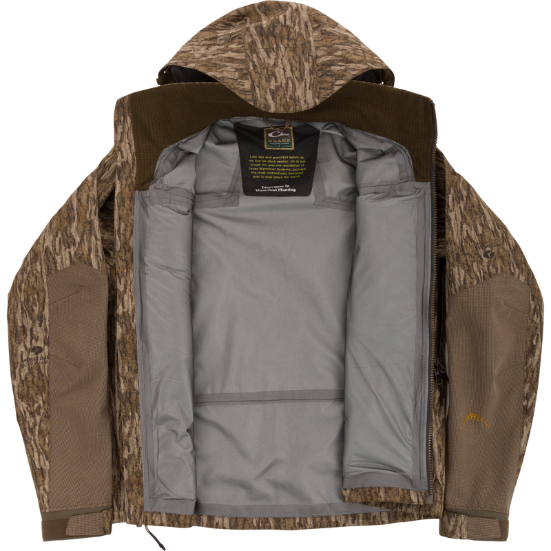 Purewhitelaneshop LST BMF Pit Jacket with camo exterior, unzipped to show gray lining and label. Designed for extreme conditions with durable, weather-resistant features.