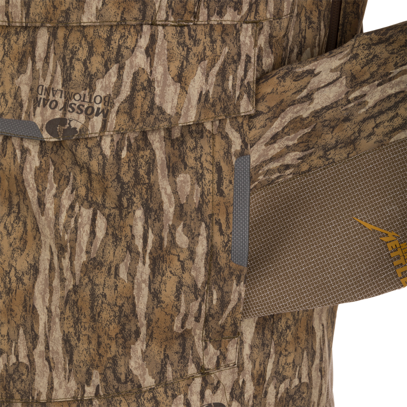 Close-up of LST BMF Pit Jacket, showcasing Mossy Oak Bottomland camo print and brown YETI strap, highlighting its durable, weather-resistant fabric and functional design for extreme conditions.