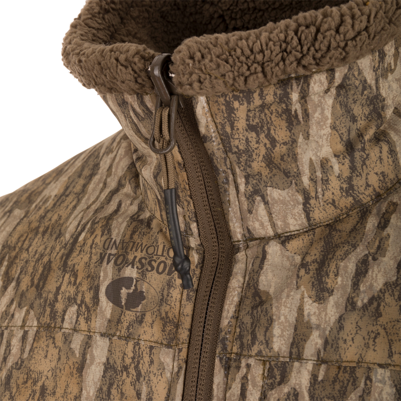 Close-up of the LST BMF 3-in-1 Pit Jacket with Primaloft, featuring Mossy Oak Bottomland camo, front zipper, and fleece-lined collar for enhanced warmth and durability.