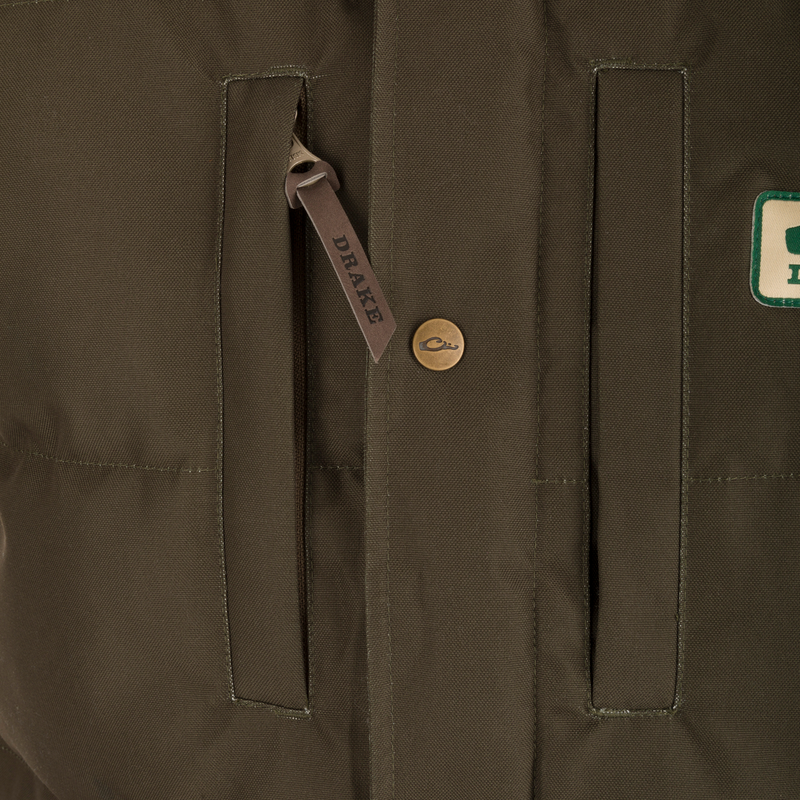 Close-up of Drake's Throwback 80 Featherless Puffer Jacket, featuring vertical welt pockets, embossed brass snap, and leather zip pull tab stamped “DRAKE.”