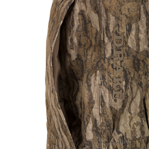 Close-up of a DRAKE LST Hardline Insulated Bib, showcasing camo-patterned shell, seam detail, and a pocket for optimal warmth and weather protection.