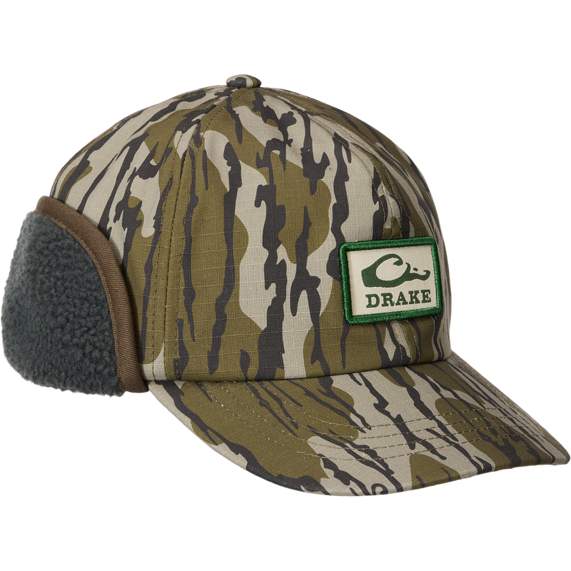 Camouflage MST Flap Cap with fold-down fleece ear flaps, featuring a DRAKE patch with a duck head. Made from durable cotton canvas, ideal for outdoor adventures.