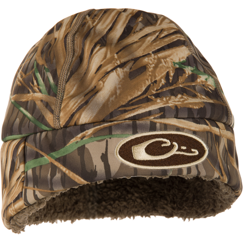 Camouflage-patterned Drake LST Windstopper Beanie with embroidered logo, featuring fleece lining and windproof membrane, designed to cover ears for warmth and comfort during waterfowl hunting.