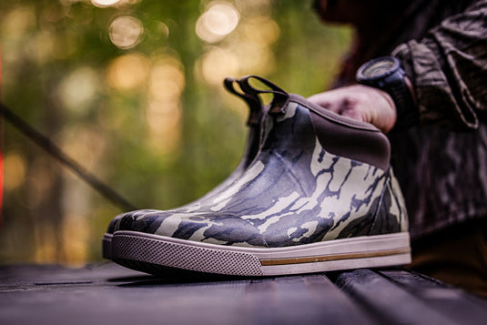 Camouflage-patterned shoe being held by a person outdoors