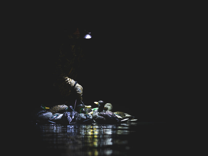 Lumen Camo Headlamp EVO1500 worn by person on rocks, featuring powerful light for hunting, with rugged design and adjustable headband. Ideal for outdoor adventures.