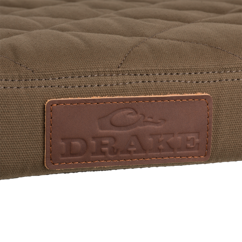 Close-up of the Team Gun Dog Landing Zone Quilted Canvas Dog Bed's olive-brown surface with DRAKE embossed leather label, showcasing its rugged, water-resistant design.