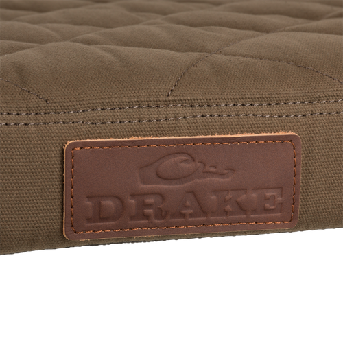 Close-up of the Team Gun Dog Landing Zone Quilted Canvas Dog Bed's olive-brown surface with DRAKE embossed leather label, showcasing its rugged, water-resistant design.