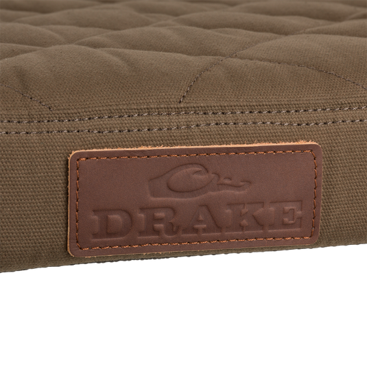 Close-up of the Team Gun Dog Landing Zone Quilted Canvas Dog Bed's olive-brown surface with DRAKE embossed leather label, showcasing its rugged, water-resistant design.