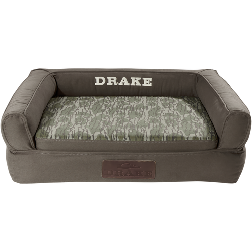 Team Gun Dog Landing Zone Premium Canvas Dog Couch with olive-drab cover, camouflage cushion, and embroidered DRAKE branding, featuring three-sided bolster and slip-resistant bottom.